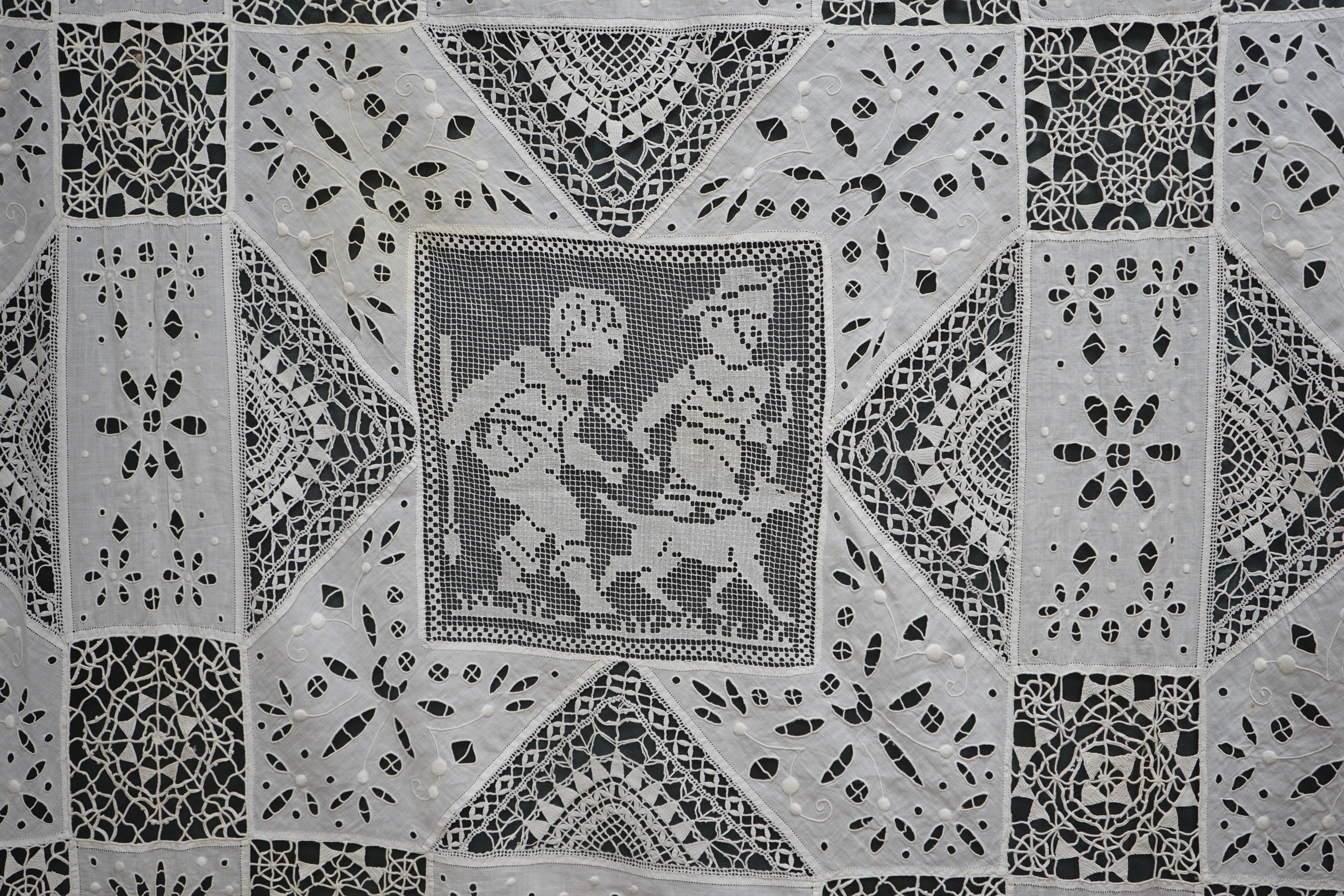 An early 20th century Italian bedcover, worked with fillet lace insertions of putti, white multi patterned fine linen cut work squares and similar multi patterned hand needle lace insertions, creating a unique and totall
